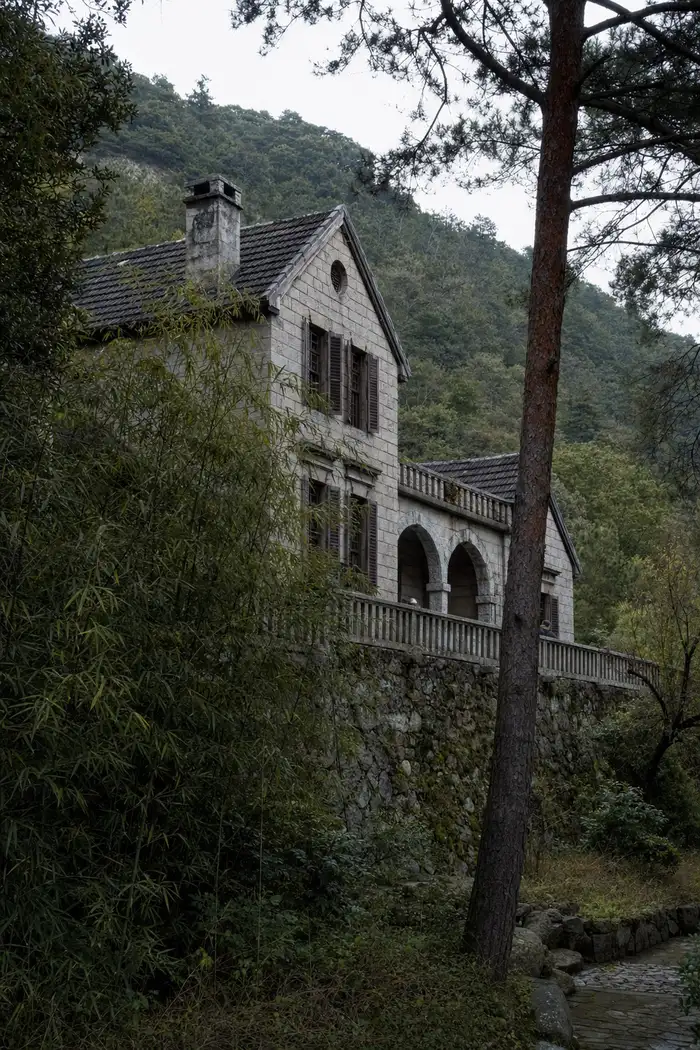 A stone villa with a shuttered veranda standing above a wooded slope