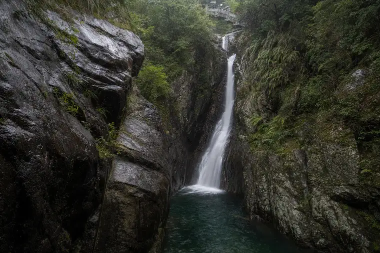 A waterfall falling into a dark pool in a rock gorge at Moganshan